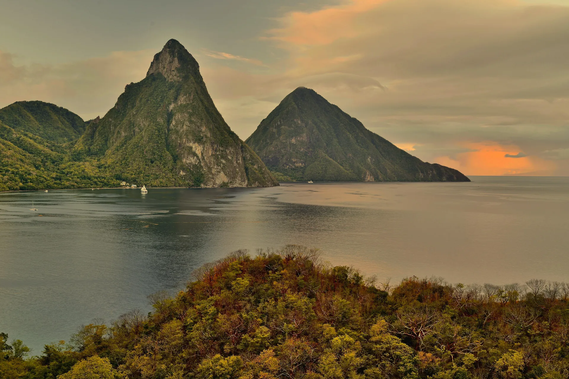 A breathtaking sunset view of the Pitons in St. Lucia with lush greenery and calm sea.